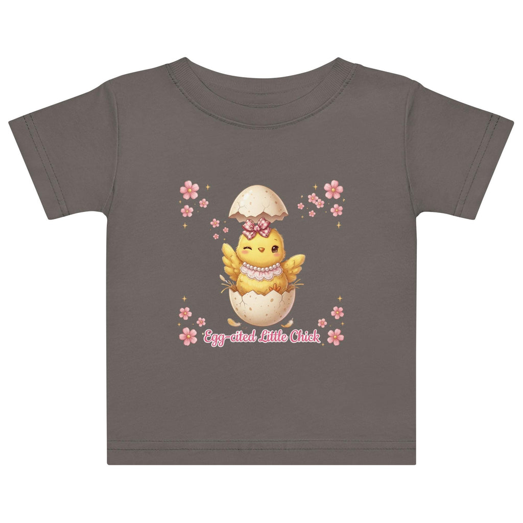 May include: White short-sleeved t-shirt featuring a cartoon chick hatching from an egg, with the text "Egg-cited Little Chick" in pink. The chick is yellow with a pink bow and necklace. The child is wearing a pink bow.