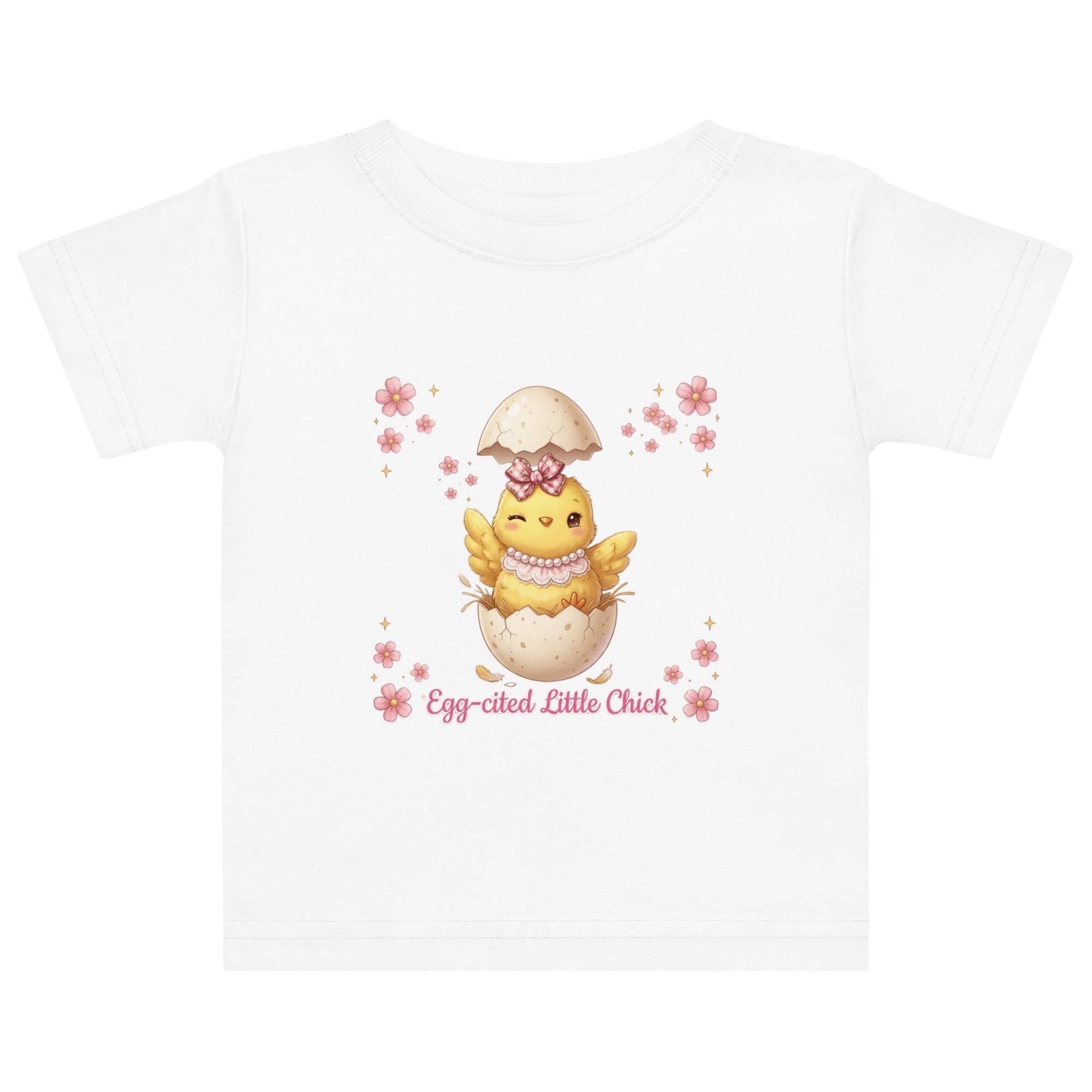 May include: White short-sleeved t-shirt featuring a cartoon chick hatching from an egg, with the text "Egg-cited Little Chick" in pink. The chick is yellow with a pink bow and necklace. The child is wearing a pink bow.