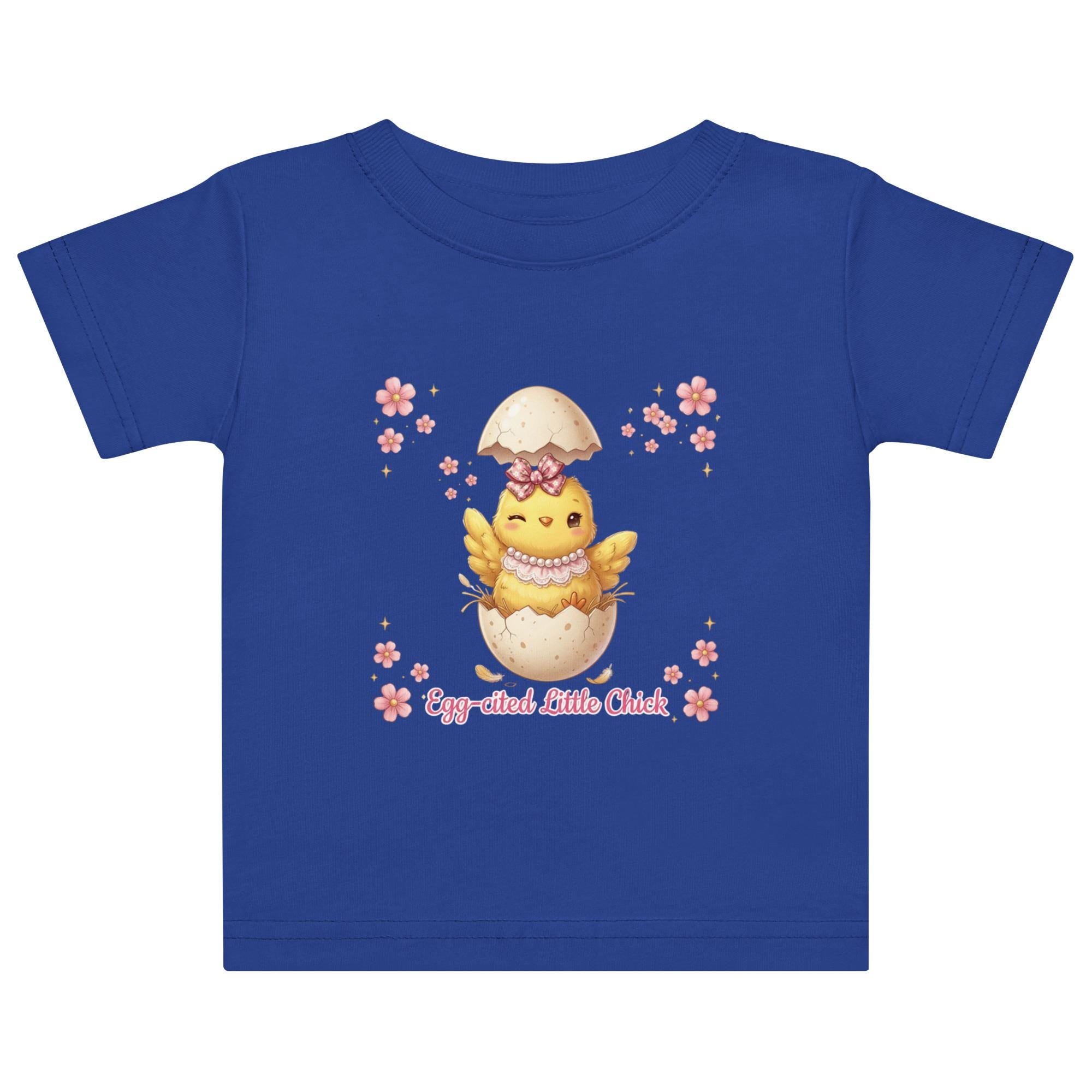 May include: White short-sleeved t-shirt featuring a cartoon chick hatching from an egg, with the text "Egg-cited Little Chick" in pink. The chick is yellow with a pink bow and necklace. The child is wearing a pink bow.