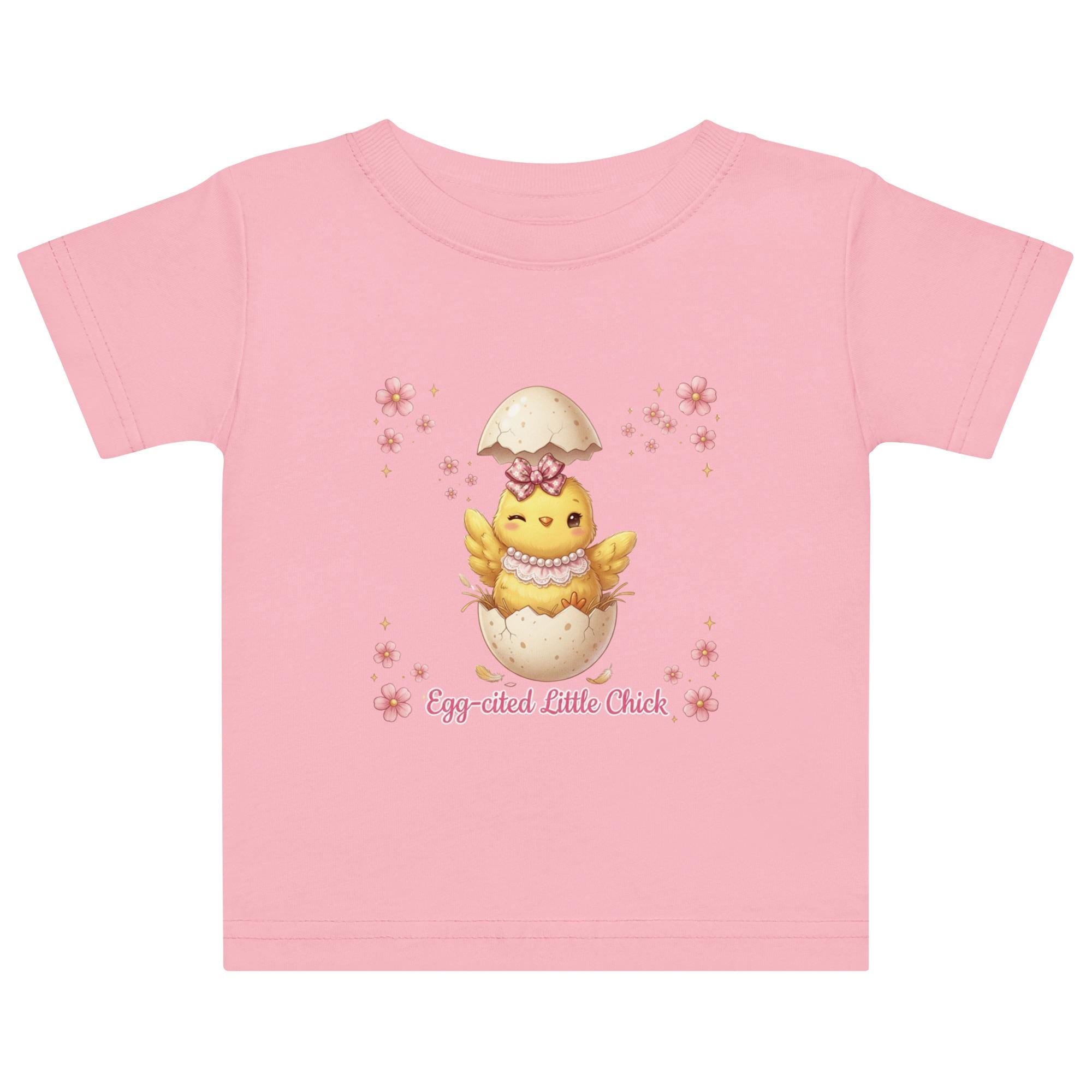 May include: White short-sleeved t-shirt featuring a cartoon chick hatching from an egg, with the text "Egg-cited Little Chick" in pink. The chick is yellow with a pink bow and necklace. The child is wearing a pink bow.