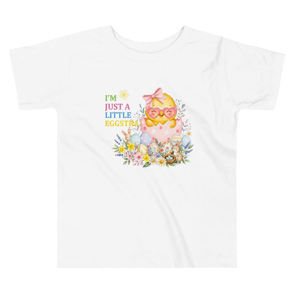 May include: A young child wearing a white t-shirt with the text "I'M JUST A LITTLE EGGSTRA" and a graphic of a chick hatching from an egg. The child is also wearing a pink tutu, pink sneakers, and white socks. The child is raising their right hand.