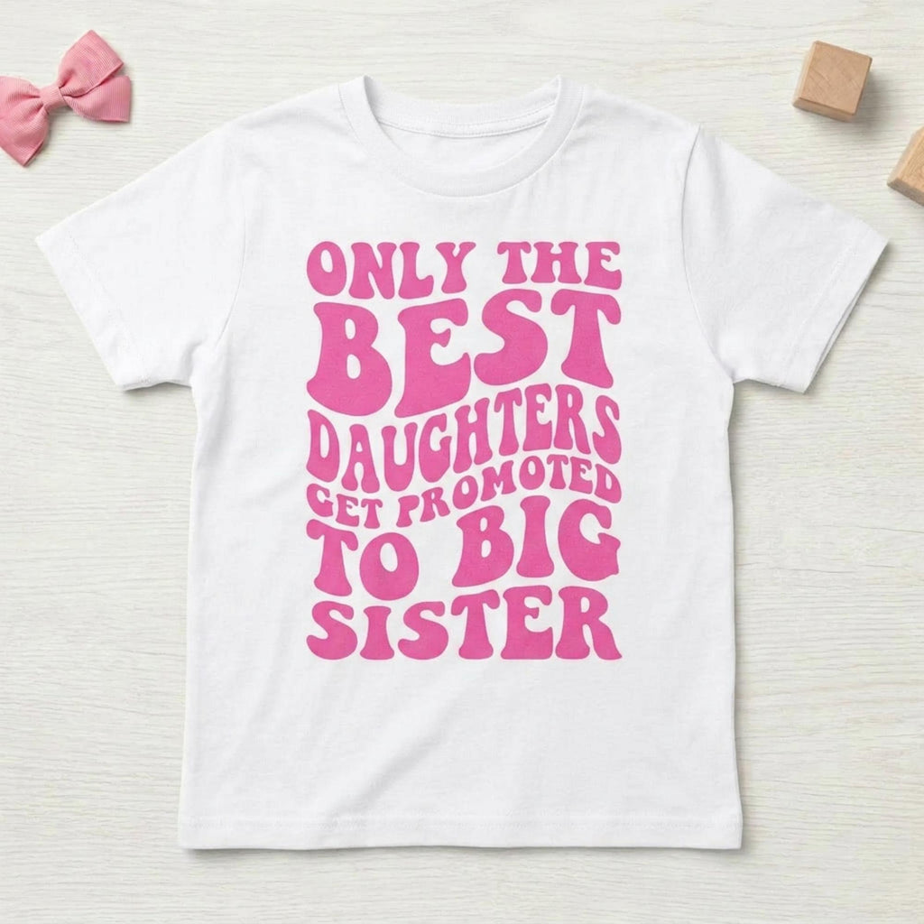 May include: White t-shirt with the text "ONLY THE BEST DAUGHTERS GET PROMOTED TO BIG SISTER" in pink, retro-style lettering. The shirt is a short-sleeved crew neck.