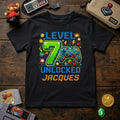 May include: Black t-shirt with a colorful video game-themed design. The design includes the text "LEVEL 7 UNLOCKED JACQUES" with a pixelated green number 7 and a game controller. Additional game-related graphics are also present.