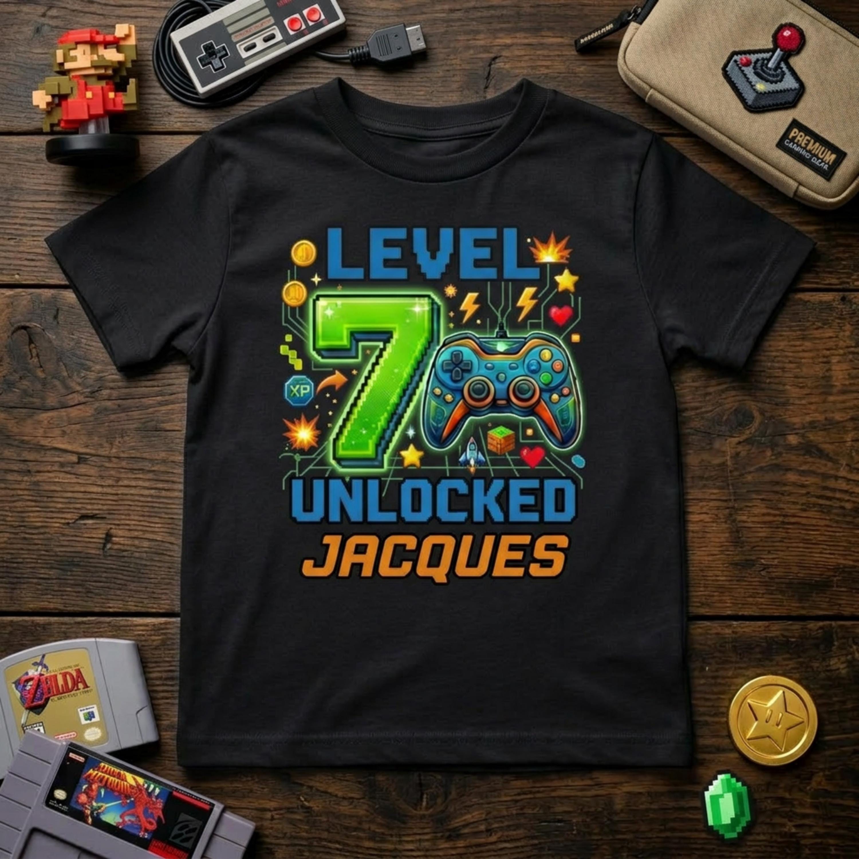 May include: Black t-shirt with a colorful video game-themed design. The design includes the text "LEVEL 7 UNLOCKED JACQUES" with a pixelated green number 7 and a game controller. Additional game-related graphics are also present.